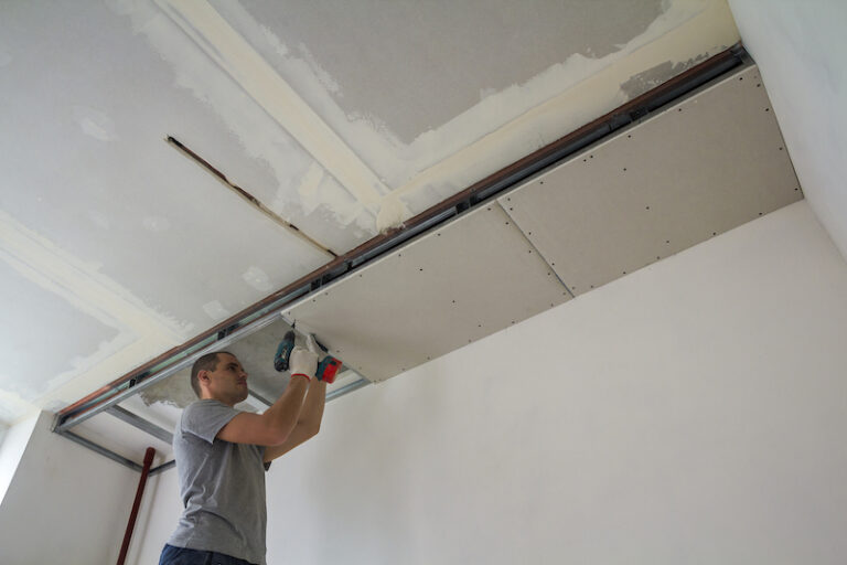 Construction worker assemble a suspended ceiling with drywall and fixing the drywall to the ceiling metal frame with screwdriver.